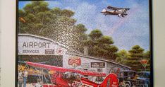 a painting of an airplane flying over a building with cars and people around it on the wall