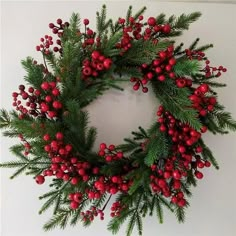 a christmas wreath with red berries and pine needles on a white background, hanging from the wall