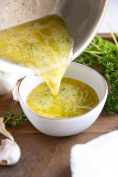 someone pouring broth into a white bowl on a cutting board next to garlic and parsley