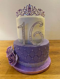 a purple and white cake with a tiara on top is sitting on a wooden table