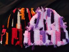 three crocheted hats are laying side by side on a black surface, one is multicolored