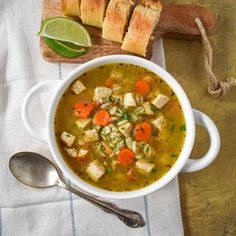 a white bowl filled with chicken soup next to sliced limes and bread on a cutting board