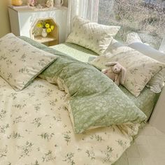 an unmade bed with green and white comforter in front of a large window