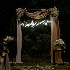 an outdoor wedding ceremony setup with flowers and draping on the arch, happily ever after