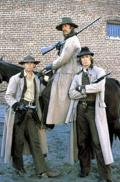 three men dressed in period clothing standing next to a horse