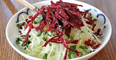 a white bowl filled with lettuce and red cabbage next to a small bowl of dipping sauce