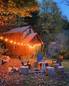 an outdoor fire pit surrounded by chairs and lights in the fall leaves near a cabin