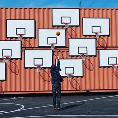 a man throwing a basketball up into the air in front of an orange shipping container