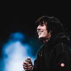 a man with long hair is smiling and holding a microphone in his hand while wearing a black hoodie