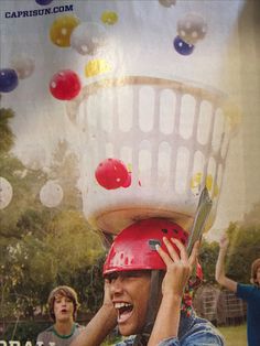 a young boy is holding up a basket on his head with balloons floating around him