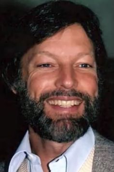 a close up of a person wearing a suit and smiling at the camera with a smile on his face