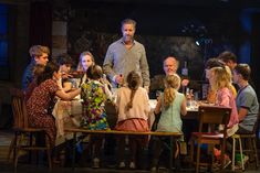 a man standing in front of a group of children sitting at a table with food