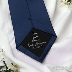 a blue tie with a black label on it and white flowers in the foreground