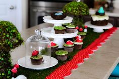 there are cupcakes on the table with moss and red ribbon around them,