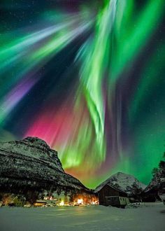 the aurora bore is shining brightly in the sky above some snow covered mountains and houses