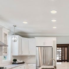 a large kitchen with white cabinets and stainless steel appliances in the center, along with marble counter tops