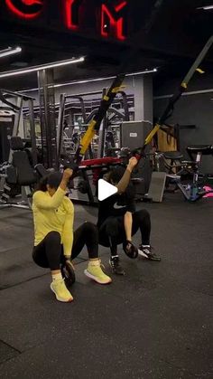 two people in a gym doing squats with one holding up the other's arm