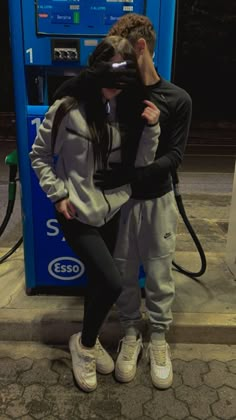 two people standing next to each other in front of a gas pump with their eyes closed