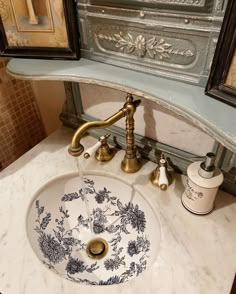 a bathroom sink with blue and white designs on the bowl, gold faucet