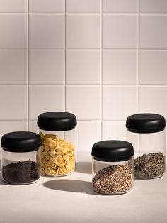 three glass jars filled with different types of food sitting on a counter top next to a white tiled wall