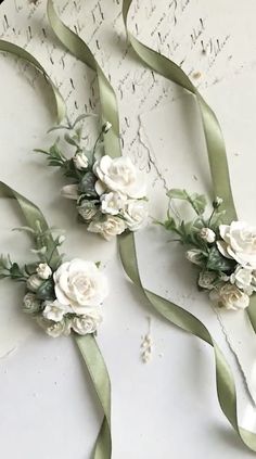 three white flowers and green ribbons on a table