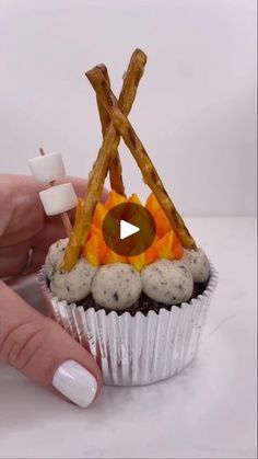 a cupcake with marshmallows and fire on top is being held by a woman's hand