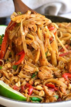 a pan filled with noodles and vegetables being lifted from the skillet by a wooden spoon