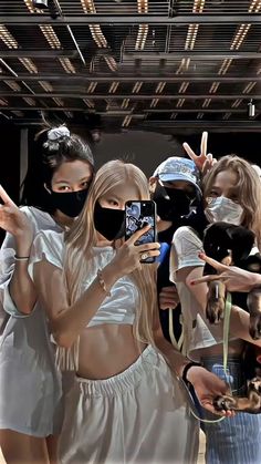 a group of people standing around each other taking pictures with cell phones and wearing face masks