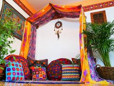 a bed covered in colorful pillows next to a potted plant