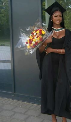 a woman wearing a graduation gown and holding a bouquet of flowers in front of a building