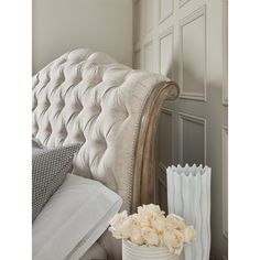 there is a white vase with flowers in it next to a bed headboard and pillows