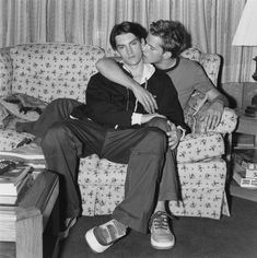 black and white photograph of two men sitting on a couch kissing each other in the living room