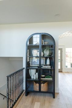 an arched glass cabinet in the entryway of a house with wood floors and railings