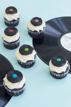 cupcakes with white frosting and black vinyl record on blue table top next to each other