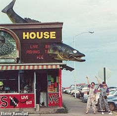 two people standing in front of a fish shop with their arms up and one person holding an umbrella