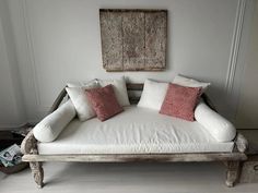 a white couch with red pillows on it in front of a wooden frame and painting