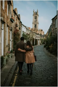 a man and woman walking down a cobblestone street in an old european town