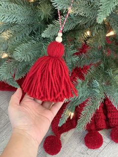 a hand holding a red tasseled ornament in front of a christmas tree