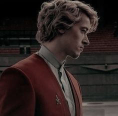 a man in a red suit and tie standing next to an empty stadium bleachers