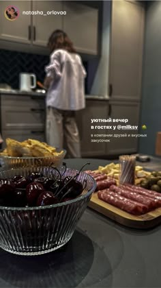 a glass bowl filled with food on top of a counter next to a woman in the kitchen