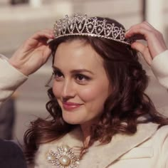 a woman wearing a tiara and smiling at the camera while holding her hair in one hand