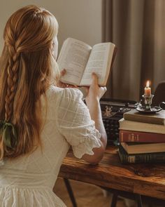 a woman sitting at a table reading a book and holding an open book in her hands