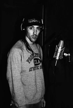 a man standing in front of a microphone wearing a sweatshirt and hat with the word's logo on it