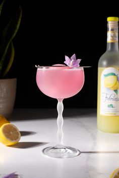 a pink drink in a glass next to some lemons