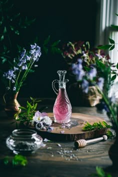 a glass bottle filled with pink liquid sitting on top of a wooden table next to flowers