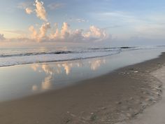 an empty beach with waves and clouds in the sky