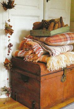 an old trunk is stacked with blankets and other decorative items in front of a white door