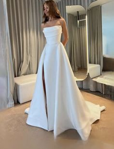 a woman standing in front of a mirror wearing a white wedding dress with high slit