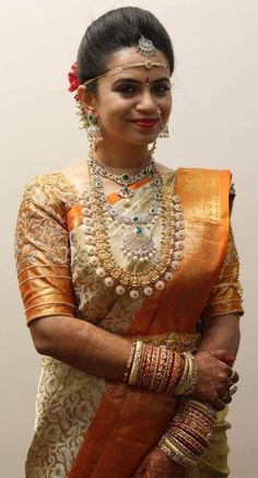 a woman in an orange and gold sari with jewelry on her head, smiling at the camera