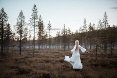 a woman in a white dress is walking through the woods with her arms spread out